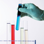 gloved hand holding test tubes with color liquid