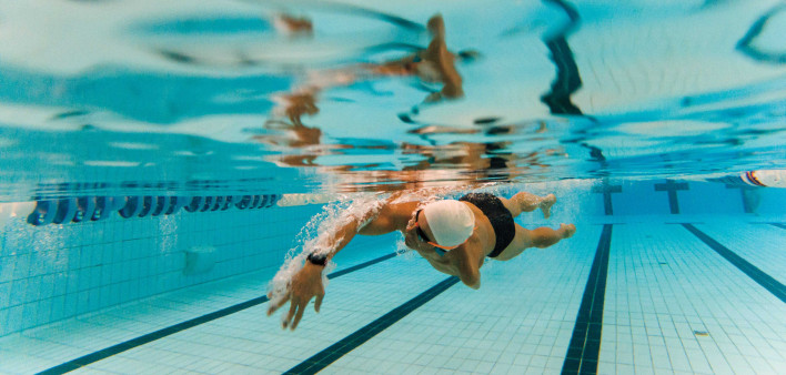 Underwater photo of an adult man with an amputated arm swimming in an indoor pool